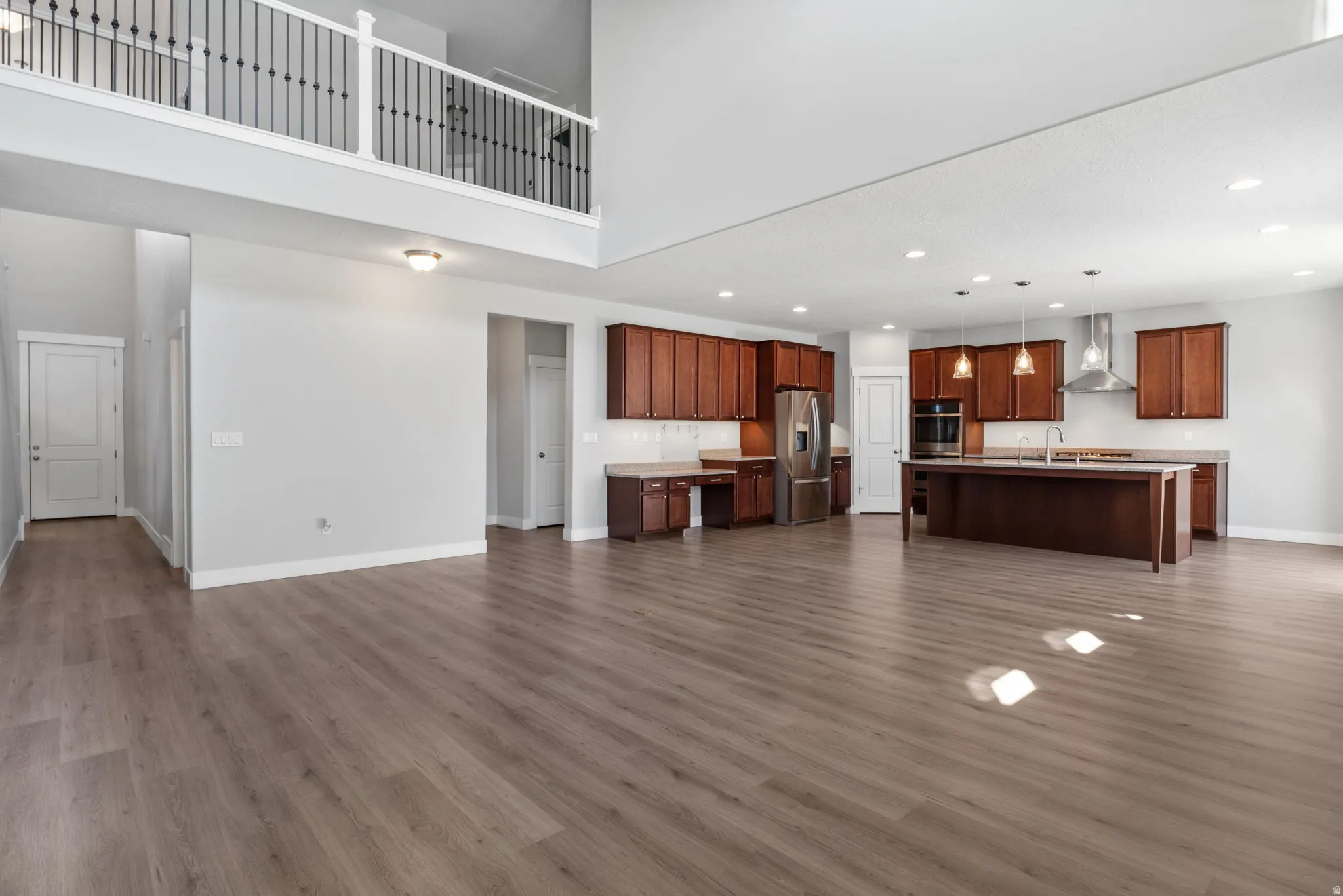Open-concept main level featuring wood-finish flooring, a two-story ceiling, and a kitchen with stainless steel appliances, a large island, and wood cabinetry