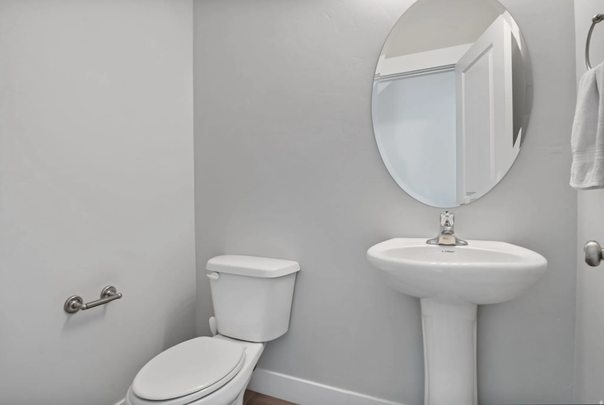 Half bath on main floor with pedestal sink, complemented by an oval wall mirror