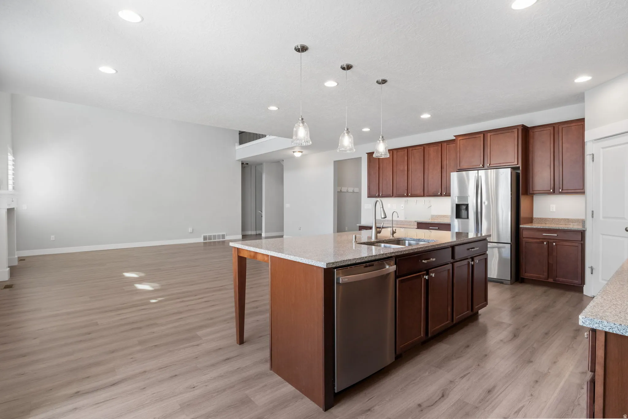 Spacious kitchen featuring an island with a double basin sink, stainless steel appliances, dark wood cabinetry, and recessed lighting