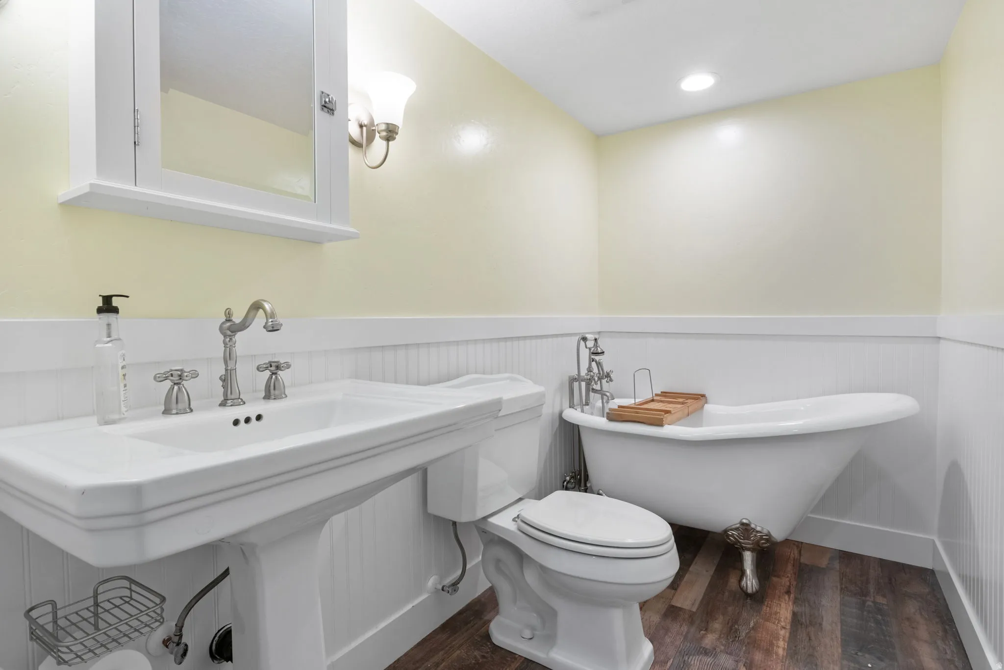 Pedestal sink, white wainscoting, clawfoot tub and wood-finish flooring. Relaxing soaker tub!