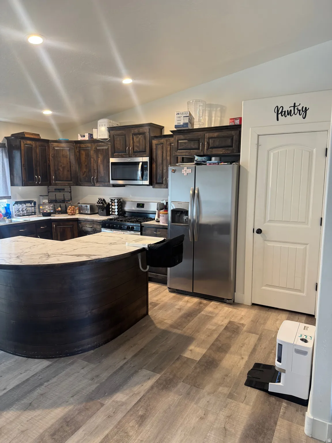 Kitchen featuring dark wood finish cabinetry, stainless steel appliances, lofted ceiling, light wood-style floors, and recessed lighting