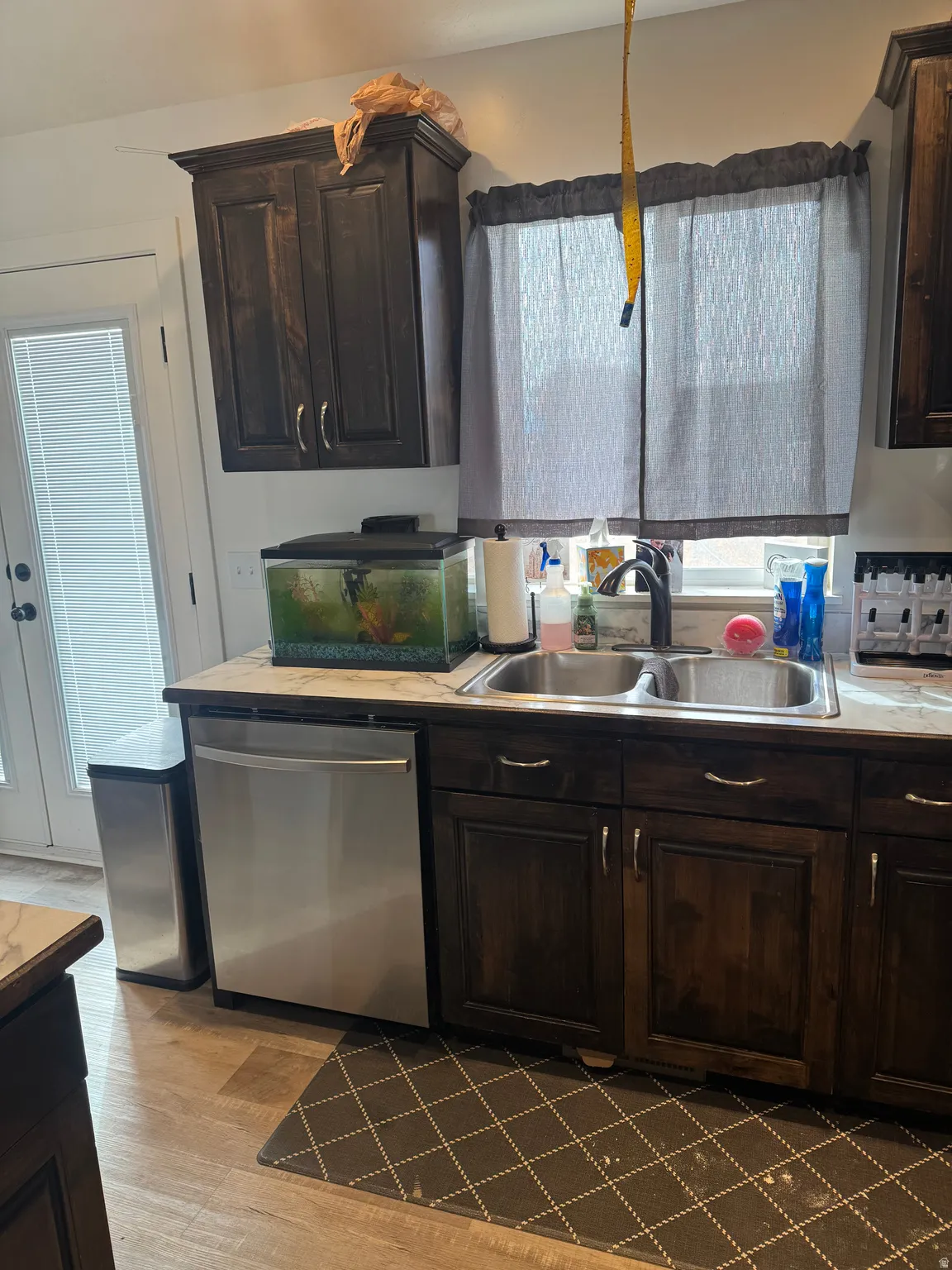 Kitchen with dark wood finish cabinetry, stainless steel dishwasher, light countertops, and light wood-style floors