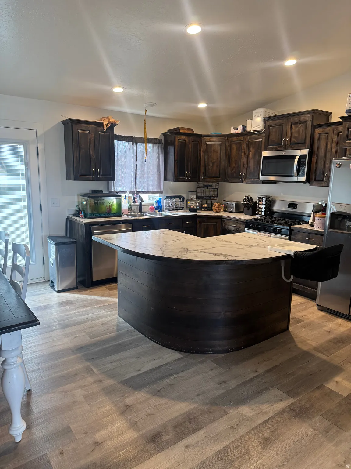 Kitchen with dark wood finish cabinets, stainless steel appliances, a kitchen island, recessed lighting, and light wood-style floors