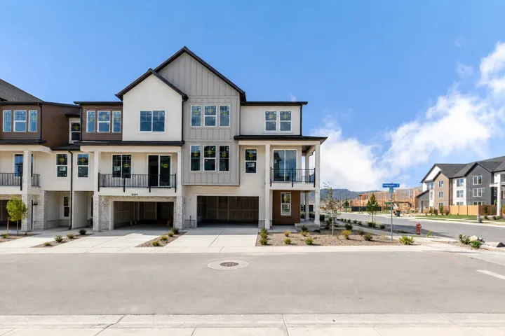 Modern townhome exterior featuring a combination of stucco and siding finishes, multiple balconies with metal railings, integrated garages, and a paved driveway