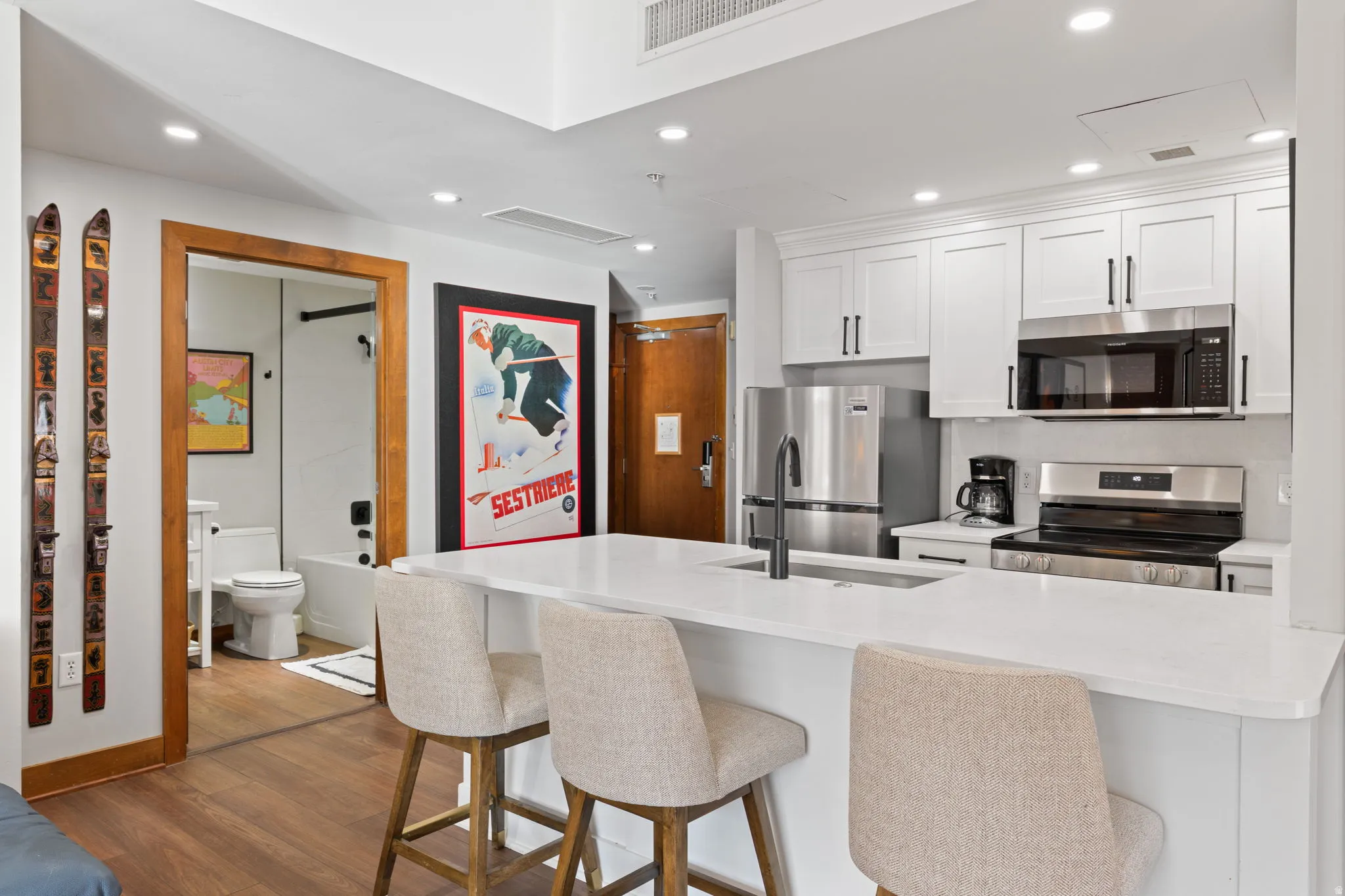 Kitchen with white cabinetry, stainless steel appliances, recessed lighting, a kitchen breakfast bar, and dark wood finished floors