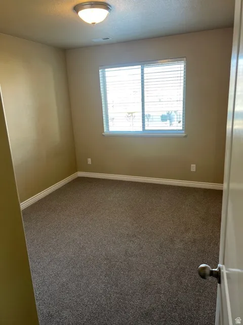 Empty room featuring dark colored carpet and a textured ceiling