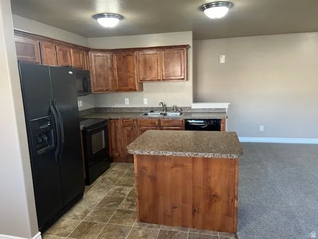 Kitchen featuring black appliances, a center island, wood finish cabinets, dark countertops, and dark stone finish floors