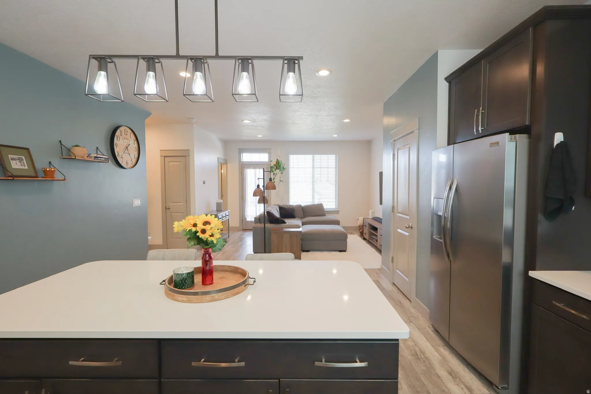 Kitchen with dark wood finish cabinets, open floor plan, stainless steel fridge, a center island, and decorative light fixtures
