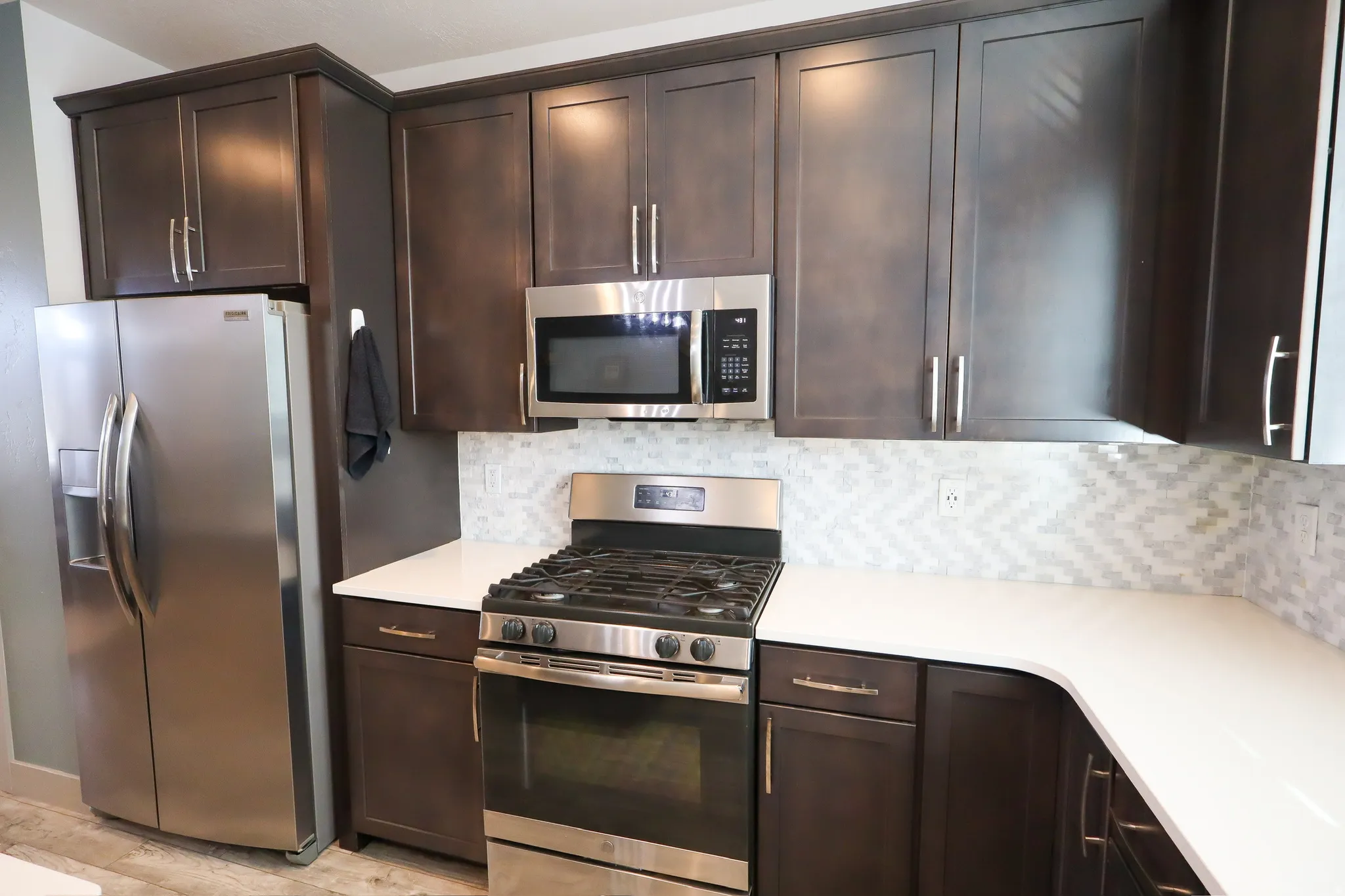 Kitchen with stainless steel appliances, dark wood finish cabinets, tasteful backsplash, and light wood finished floors