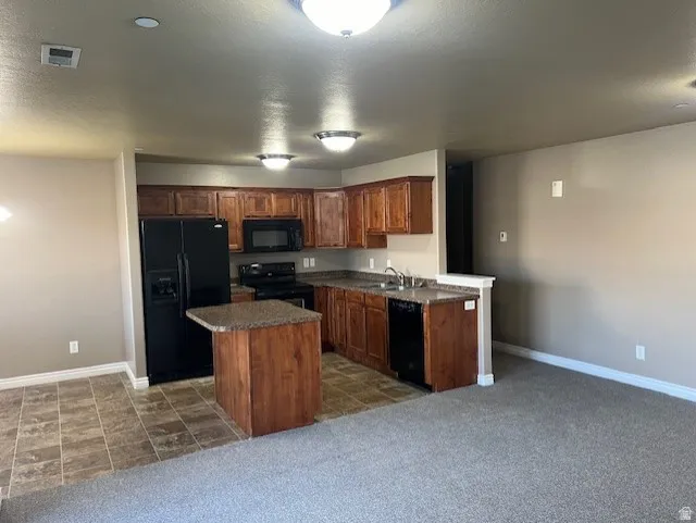 Kitchen featuring black appliances, dark countertops, a center island, dark colored carpet, and a textured ceiling