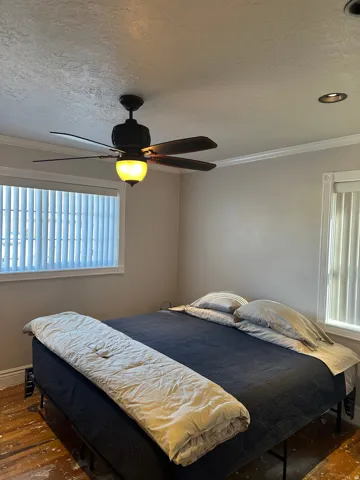 Bedroom featuring a textured ceiling, ceiling fan, wood-type flooring, and ornamental molding