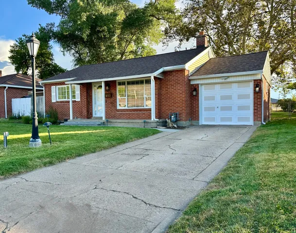 Single story home featuring concrete driveway, a shingled roof, an attached garage, brick siding, and a chimney