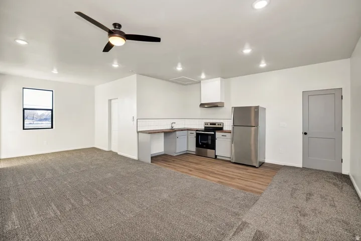Kitchen featuring stainless steel appliances, open floor plan, dark carpet, a ceiling fan, and backsplash