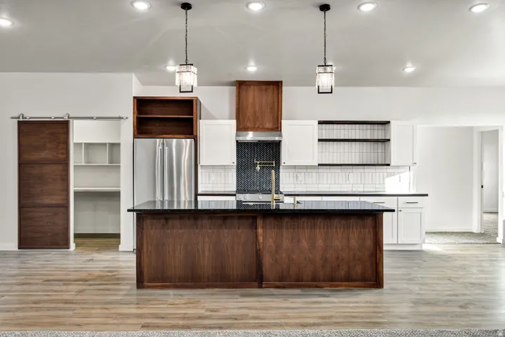 Two tone kitchen featuring open shelves, a barn door, an island with sink, light wood-style floors, and two tone color scheme