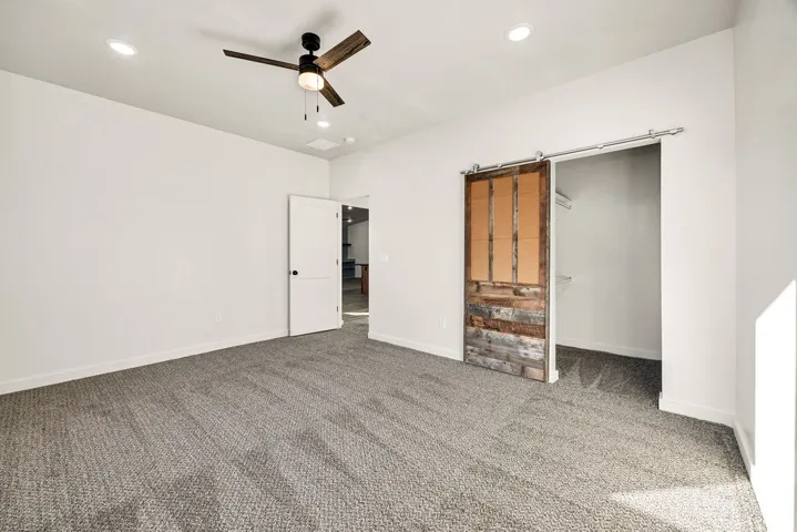 Unfurnished bedroom featuring carpet flooring, a ceiling fan, recessed lighting, a barn door, and a walk in closet
