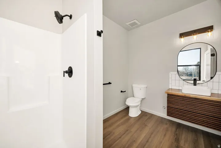 Full bathroom with vanity, dark wood-style flooring, a walk in shower, and decorative backsplash
