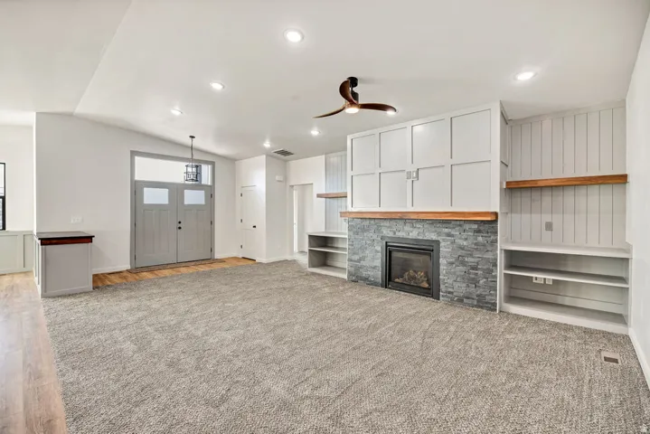 Unfurnished living room featuring ceiling fan, light colored carpet, a glass covered fireplace, recessed lighting, and vaulted ceiling
