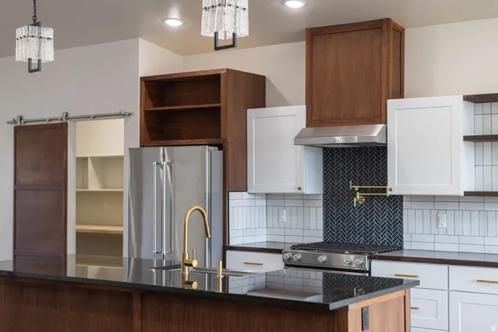 Kitchen featuring open shelves, stainless steel appliances, dark stone countertops, a chandelier, and two tone color scheme