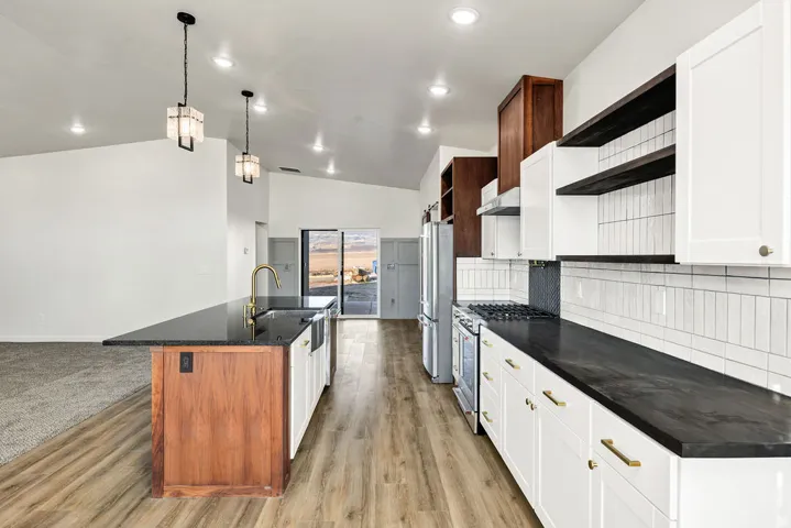 Kitchen with open shelves, vaulted ceiling, a kitchen island with sink, stainless steel appliances, and tasteful backsplash