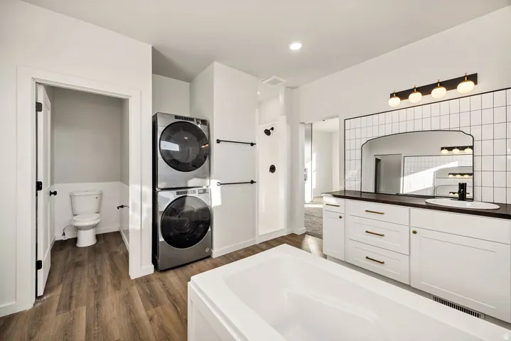 Full bath featuring vanity, dark wood-style floors, a bath, and stacked washer / dryer