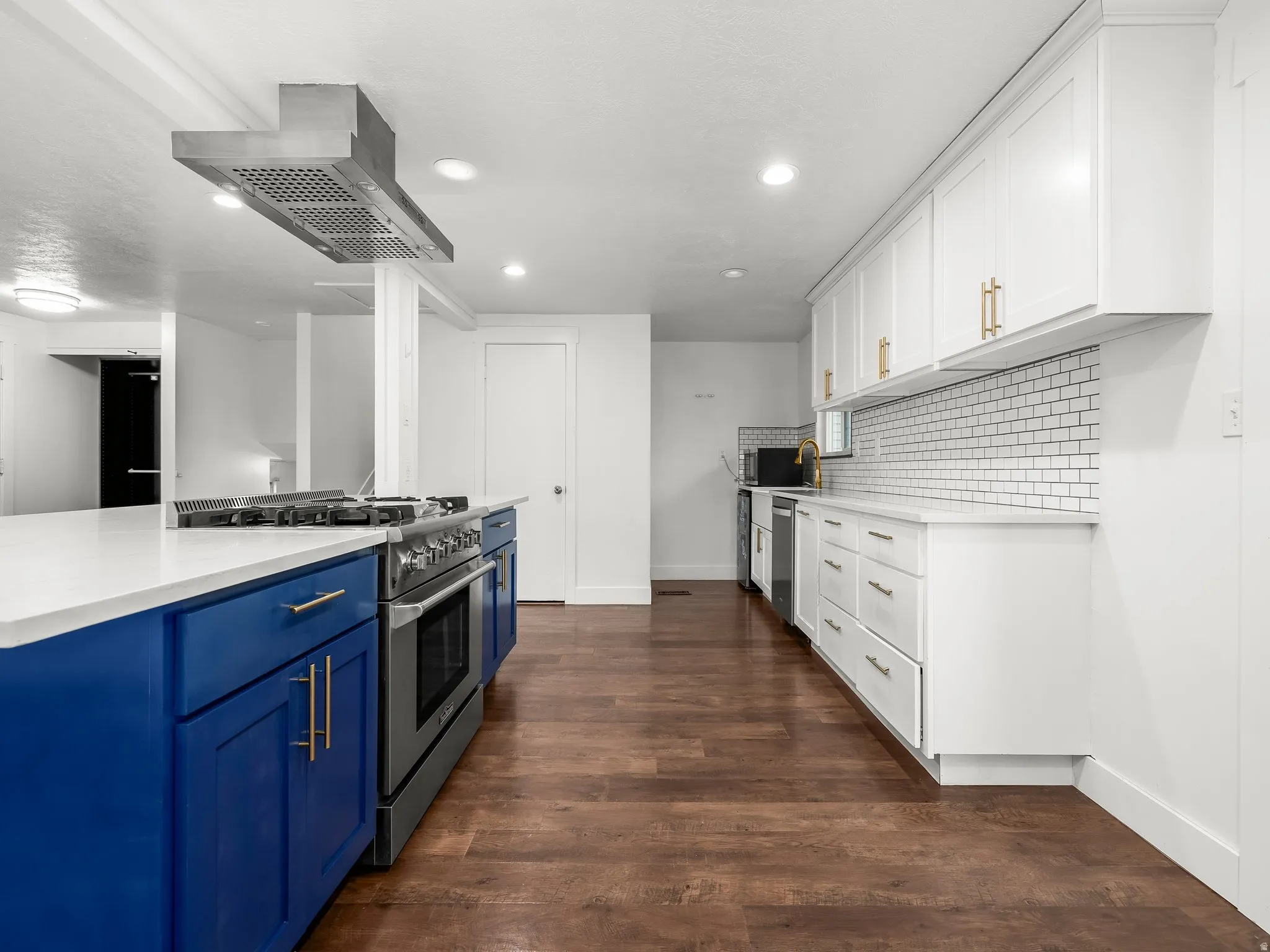 Dual tone kitchen with stainless steel appliances, two tone cabinetry, island exhaust hood, dark wood-style floors, and light stone counters