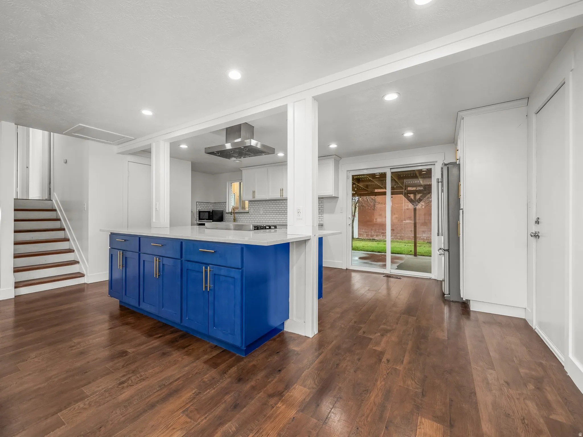 Dual tone kitchen featuring dark wood-style floors, extractor fan, light stone countertops, freestanding refrigerator, and recessed lighting
