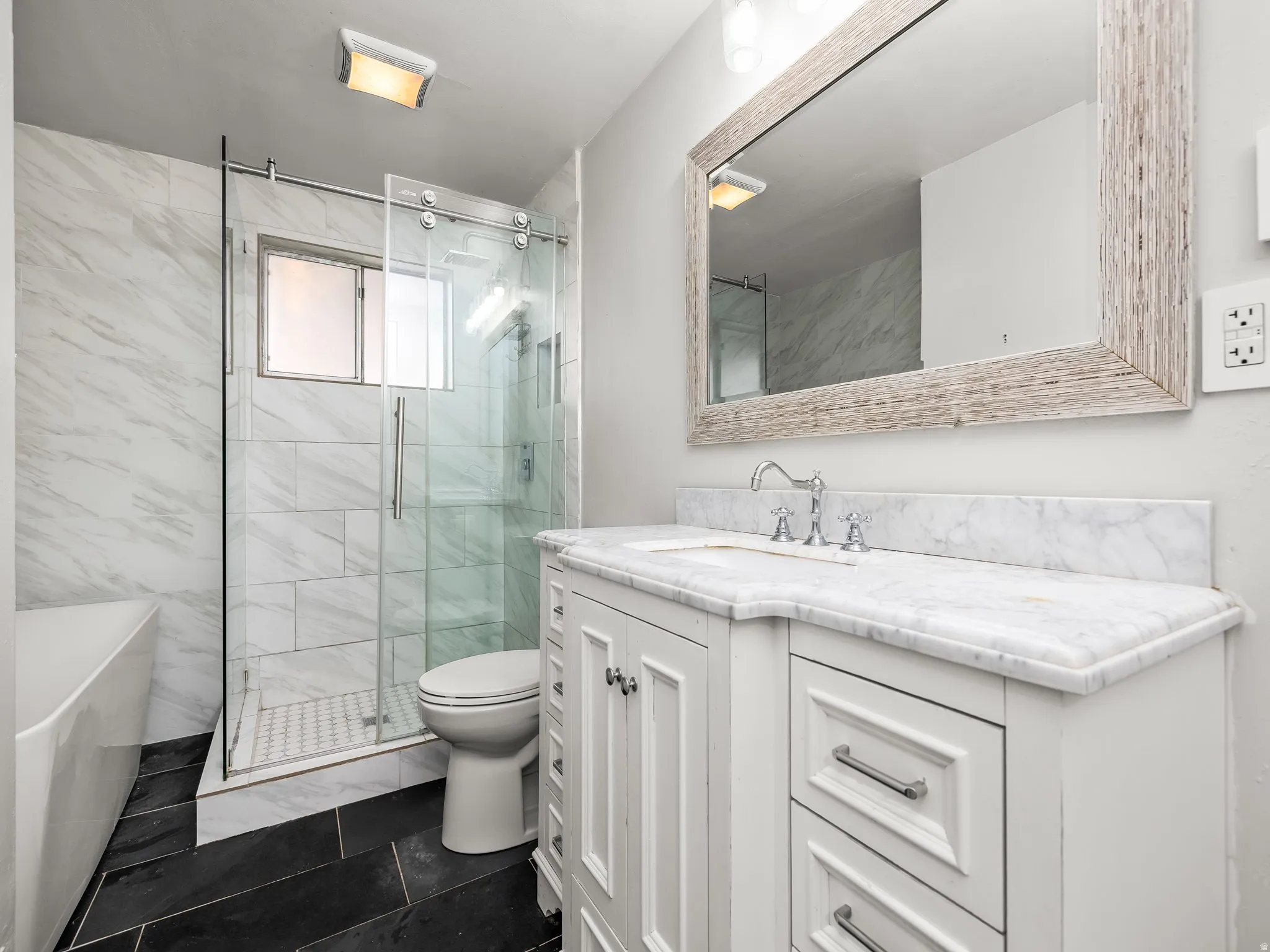 Full bathroom featuring vanity, a freestanding tub, a marble finish shower, and dark tile patterned flooring