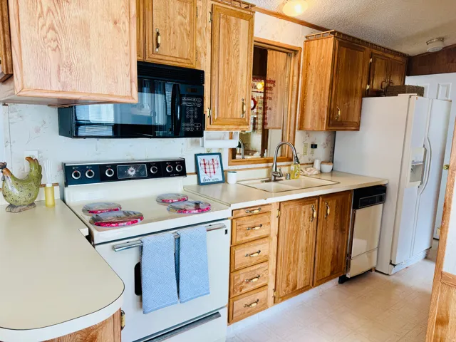 Kitchen featuring white appliances, light floors, light countertops, a textured ceiling, and wood finish cabinetry