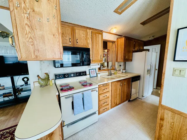 Kitchen featuring white appliances, light flooring, light countertops, a textured ceiling, and wood finish cabinets