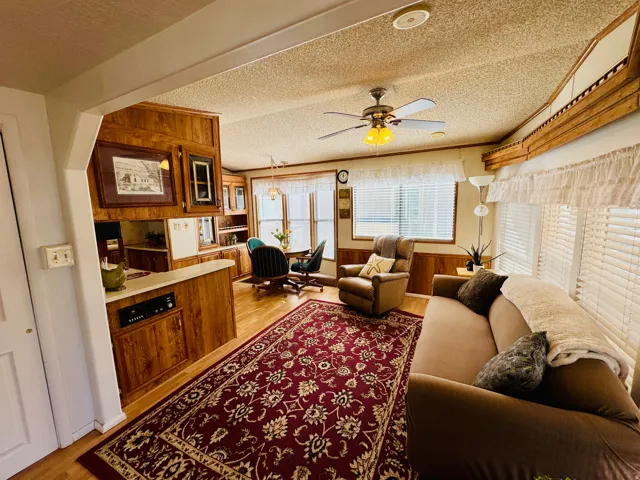 Living room with a ceiling fan, light wood-style floors, a textured ceiling, and wooden walls