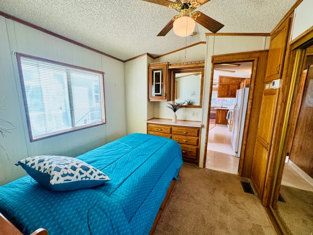 Bedroom featuring crown molding, white fridge with ice dispenser, wooden walls, carpet floors, and ceiling fan