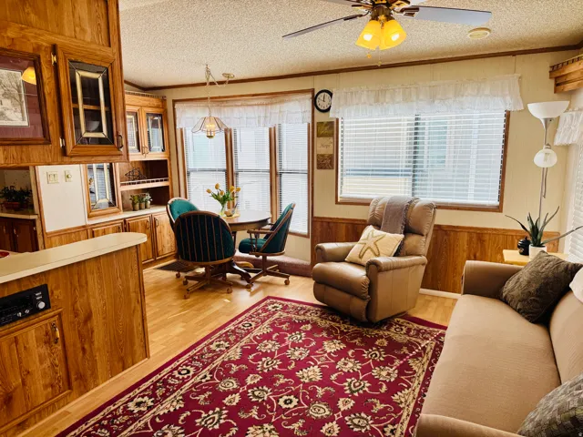 Living area featuring wooden walls, ornamental molding, wainscoting, light wood-style flooring, and a textured ceiling