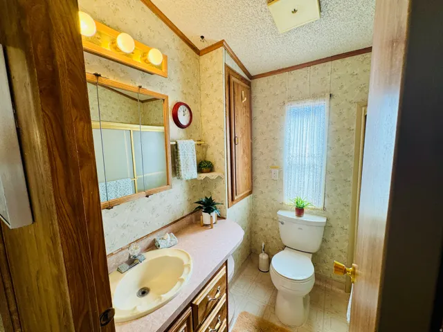 Bathroom featuring wallpapered walls, vanity, crown molding, and light flooring
