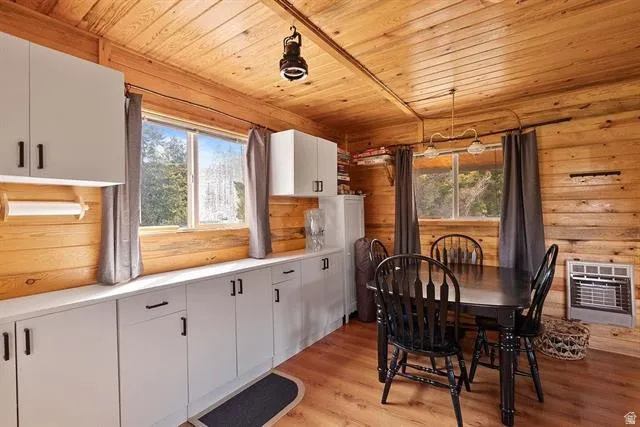 Dining room with light wood-type flooring, heating unit, wooden ceiling, and wooden walls