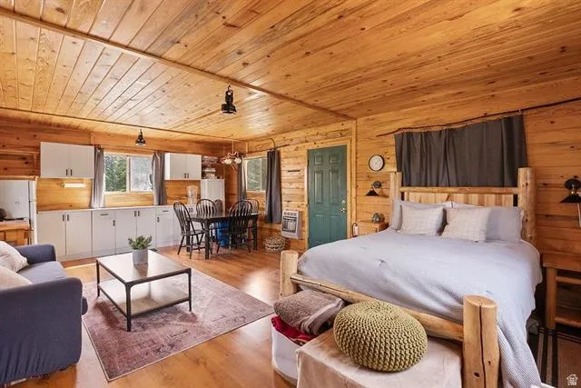 Bedroom with wooden ceiling, light wood-type flooring, heating unit, freestanding refrigerator, and wood walls