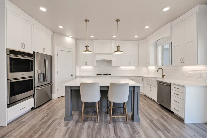 Kitchen with a kitchen island, two tone cabinetry, a breakfast bar area, stainless steel appliances, and pendant lighting
