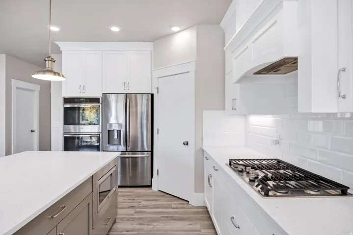 Kitchen with stainless steel appliances, decorative light fixtures, light wood-style flooring, two tone cabinetry, and light stone countertops