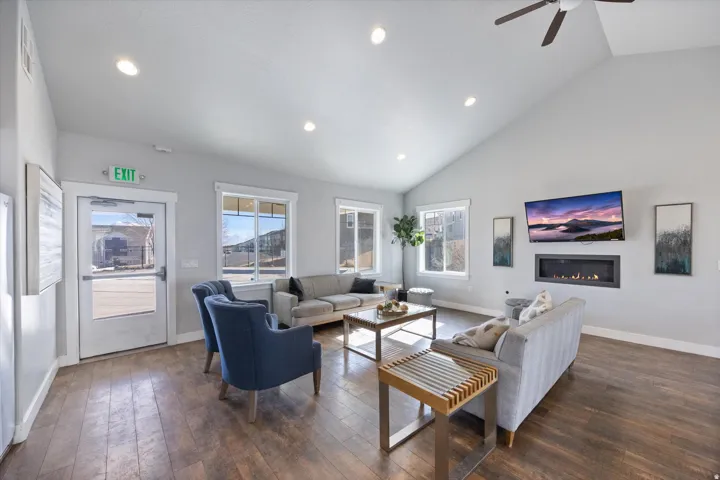 Living room featuring dark wood-style flooring, a glass covered fireplace, a ceiling fan, lofted ceiling, and recessed lighting