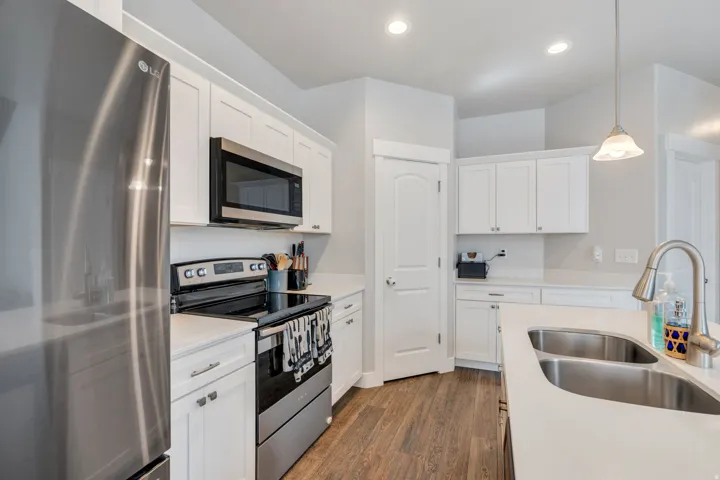 Kitchen featuring stainless steel appliances, white cabinetry, hanging light fixtures, dark wood finished floors, and light stone countertops