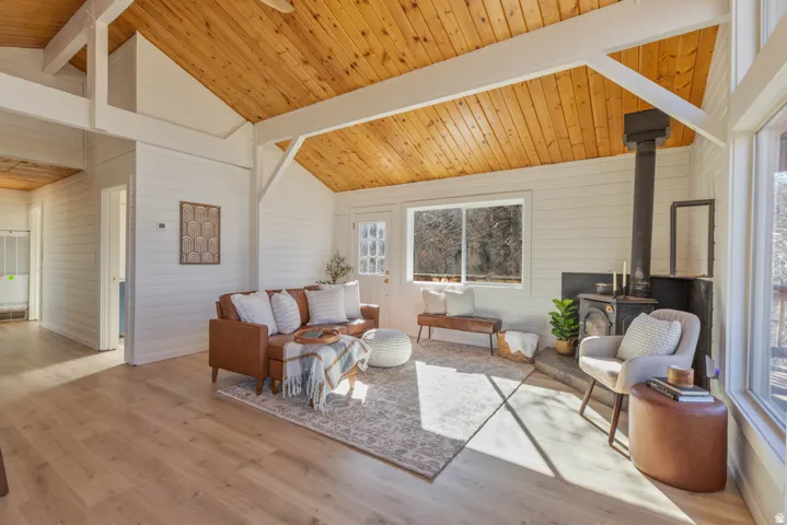 Living area featuring a wood stove, light wood-type flooring, a high wood beamed ceiling, and wood walls