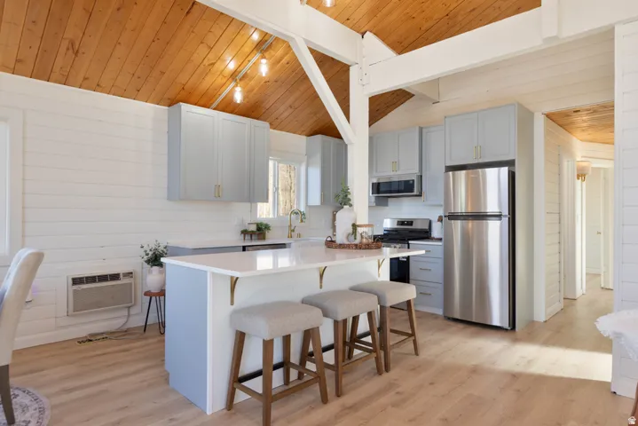 Kitchen with stainless steel appliances, a breakfast bar, gray cabinetry, light wood finished floors, and wood walls