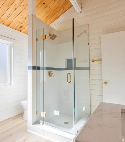 Full bath with a stall shower with frameless glass,  a vaulted wooden ceiling, wood walls, and wood finished floors