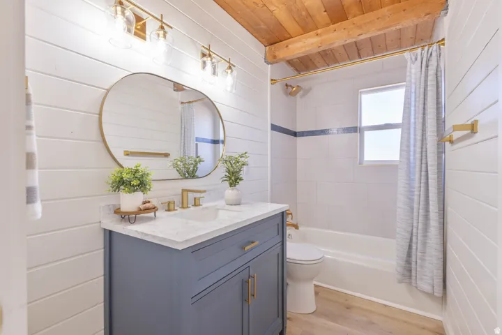 Bathroom featuring a wooden ceiling with exposed beams, vanity, light wood finished floors, wood walls, and shower / bath combination with curtain