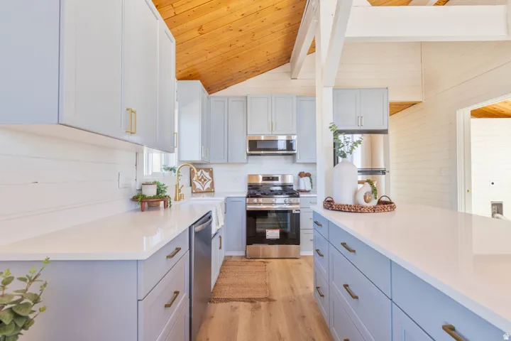 Kitchen featuring stainless steel appliances, wood ceiling, light wood-style floors, dual tone cabinetry, and vaulted ceiling with beams