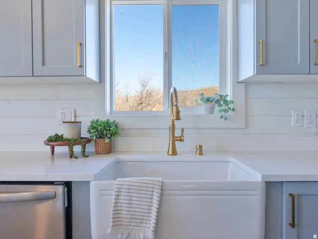 Kitchen view of stainless steel dishwasher, light stone counters, and white cabinetry
