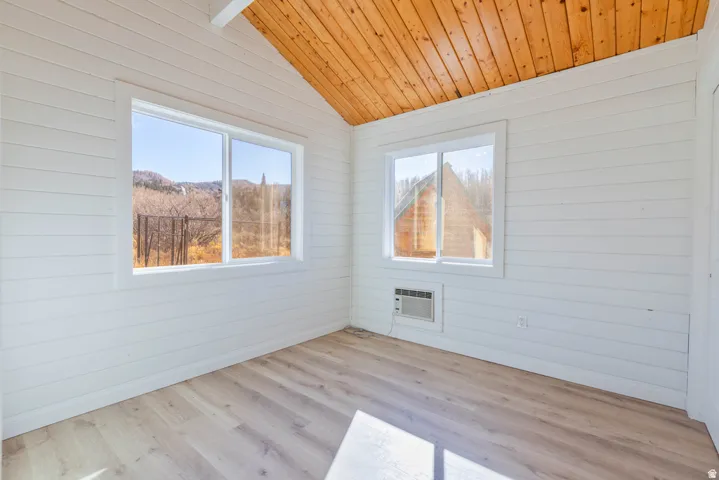 Empty room with healthy amount of natural light, light wood-style flooring, a vaulted wooden ceiling, and wood walls
