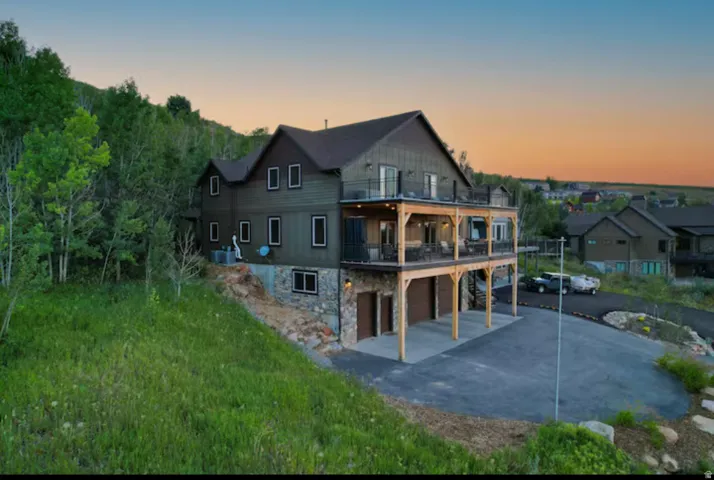 Back of property with stone siding, a patio area, an attached garage, driveway, and a balcony