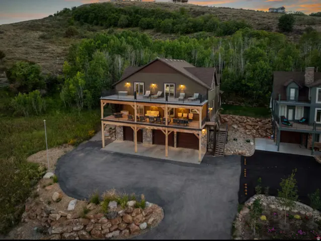 Back of house at dusk with stone siding, driveway, a patio area, a garage, and a balcony