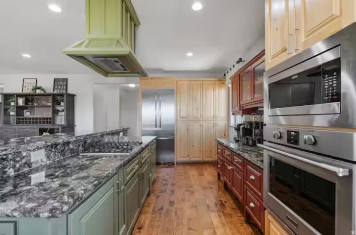 Dual tone kitchen featuring dark stone countertops, built in appliances, light wood finished floors, two tone cabinetry, and glass fronted cabinets