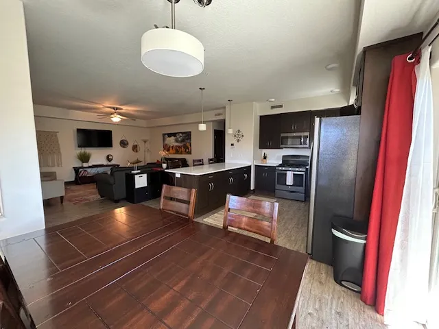 Kitchen featuring stainless steel appliances, light countertops, open floor plan, hanging light fixtures, and ceiling fan